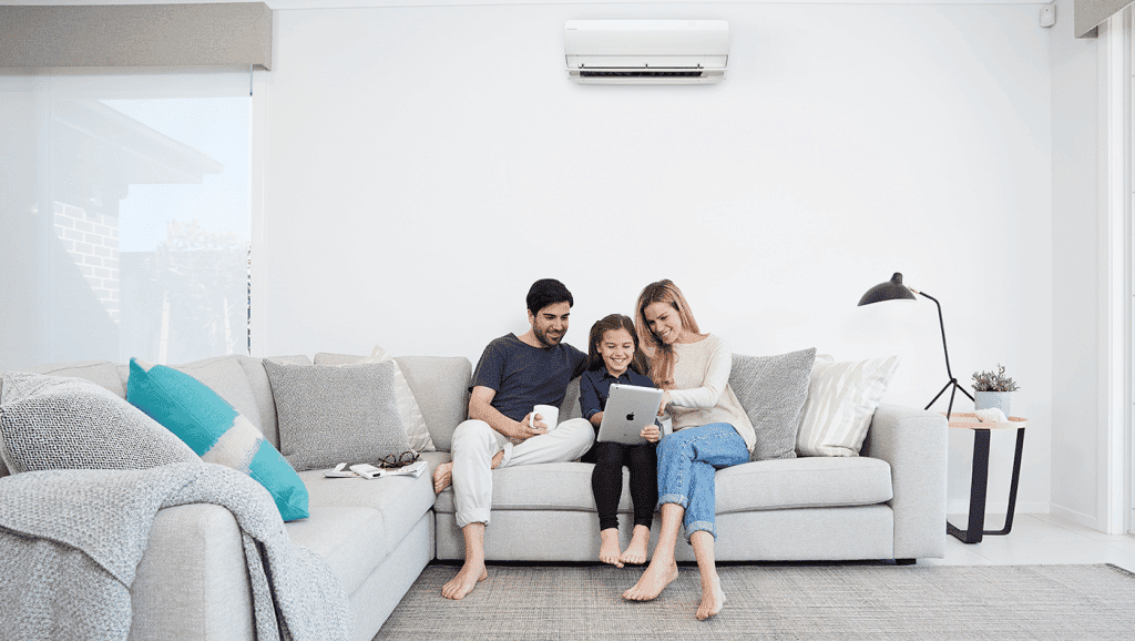 family of three sitting on couch with air conditioner above